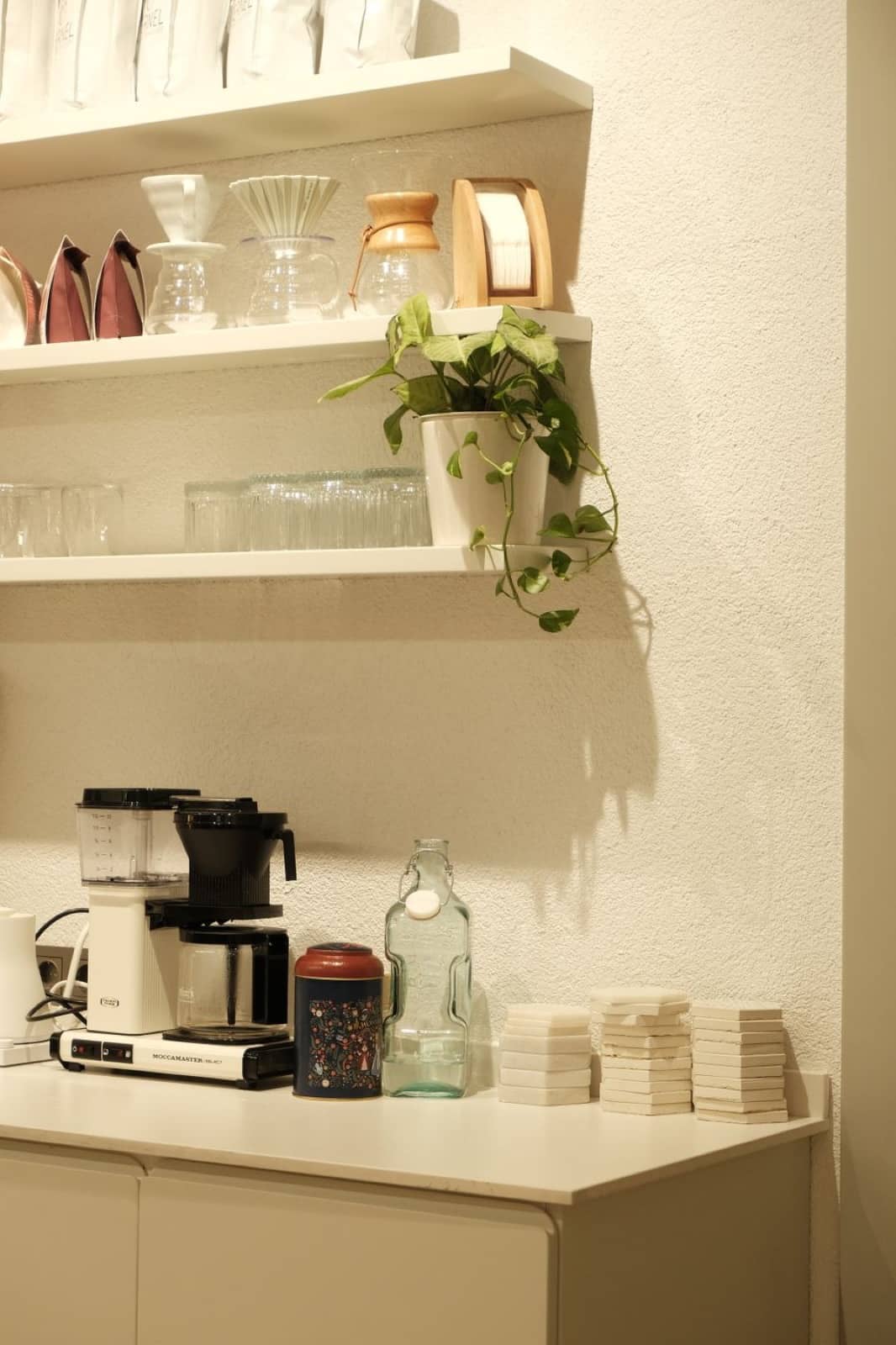 A tidy coffee station with a coffee maker, mugs, and glassware, stocked and ready
